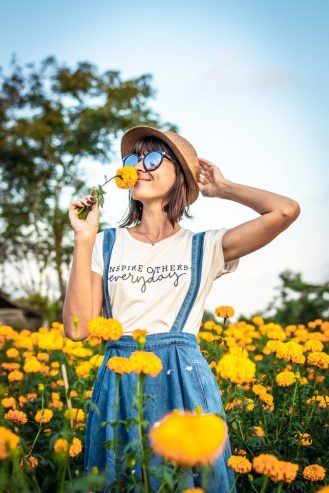 woman holding a hat and smelling a yellow flower