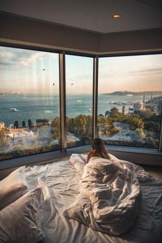 woman laying down in bed while looking at the view outside