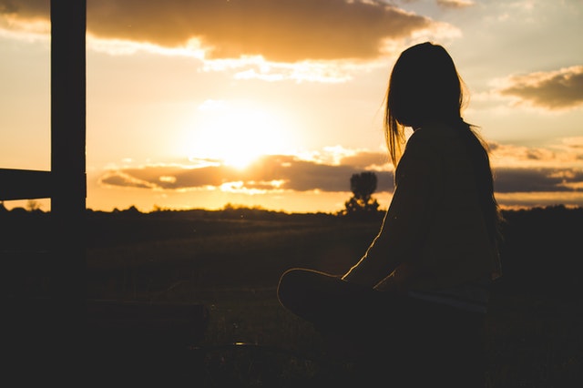 silhouette photo of woman sitting near trees during golden hour