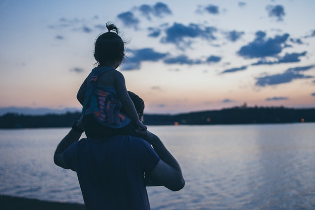 man carrying his daughter on his shoulder looking at the sea