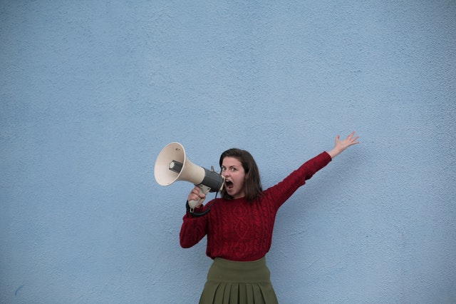 angry woman yelling into loudspeaker on blue background