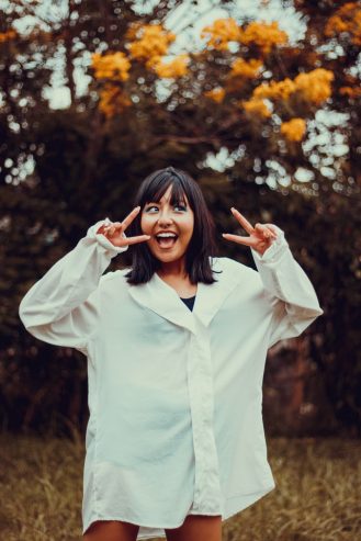 excited young ethnic woman showing two fingers gesture in park